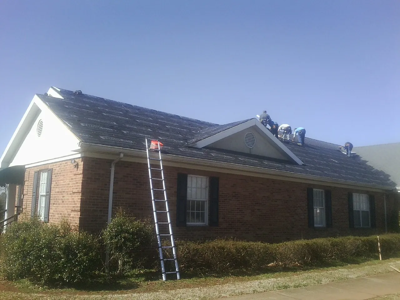 Crew tearing shingles off a brick ranch roof with a ladder set — Emergency Roof Repair work by our crew in Dexter