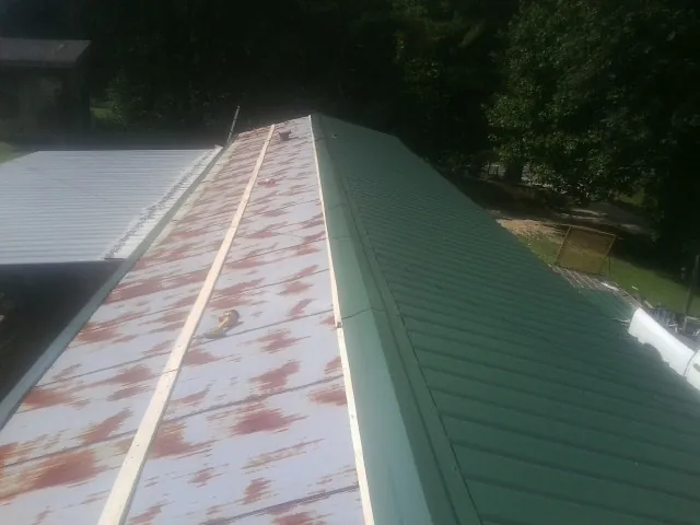 Old rusted panels beside newly installed green metal roofing — Wind Damage Roof Repair by Roofing Brothers in Dexter